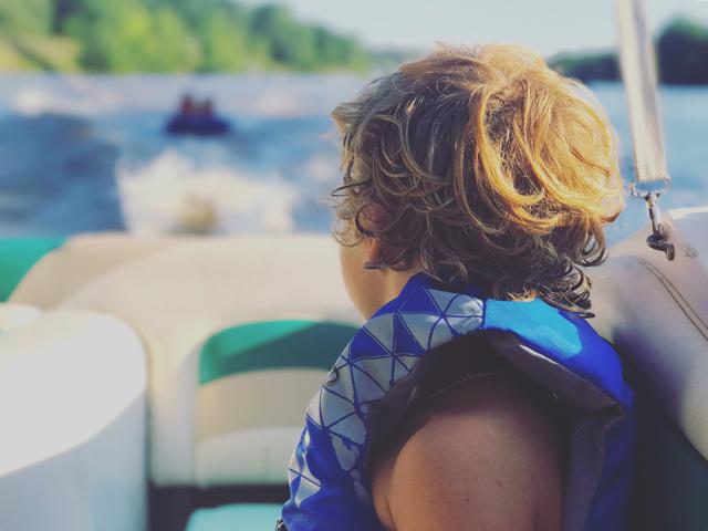 A boy wears a life jacket and looks behind the boat, California boating concept.