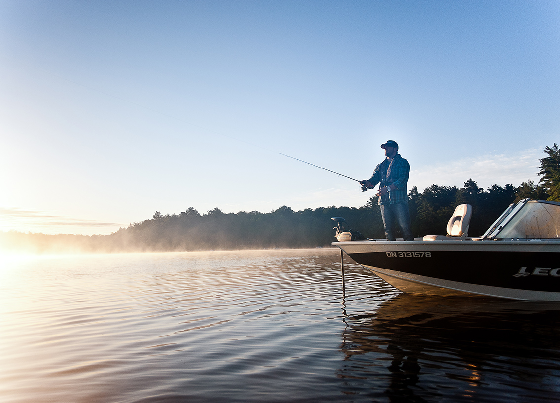 A man fishing from the front of a boat on a lake, boating in Vermont concept.