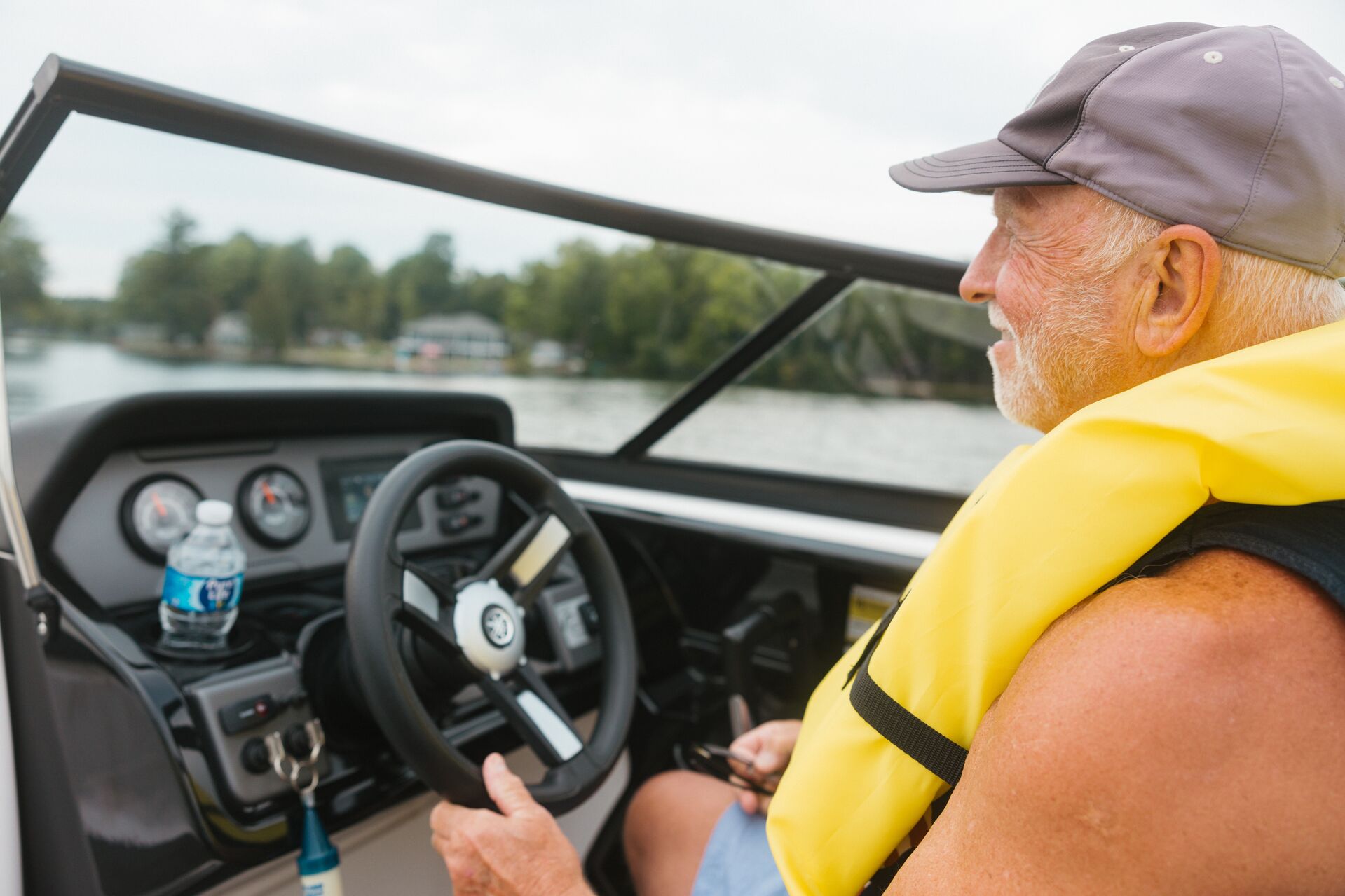 A man wears a yellow life jacket while driving a boat on a lake.