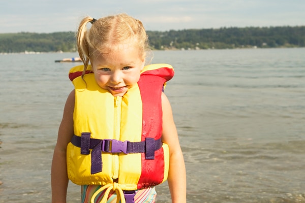 A small child in a life jacket near a body of water.