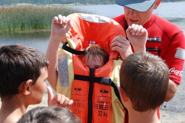Image of a man teach children how to properly fit a life jacket.