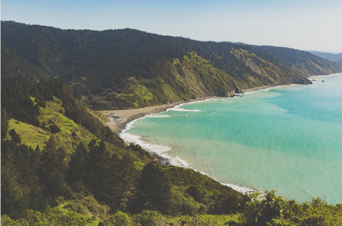 Overlooking a beach and water with surrounding hills.