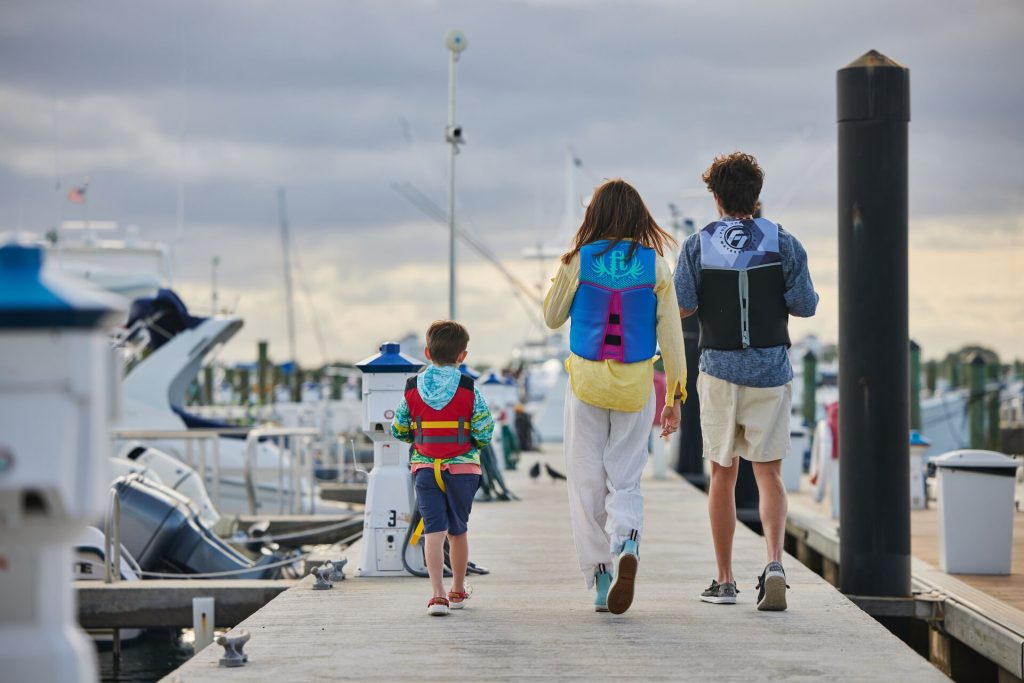 Kids walking on the dock while wearing life jackets at a marina.