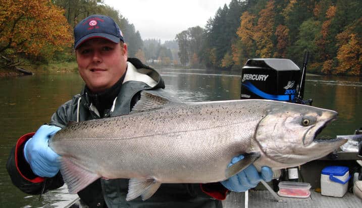A man holds a big salmon he just caught while on a boat, represents what you can catch when fall fishing. 