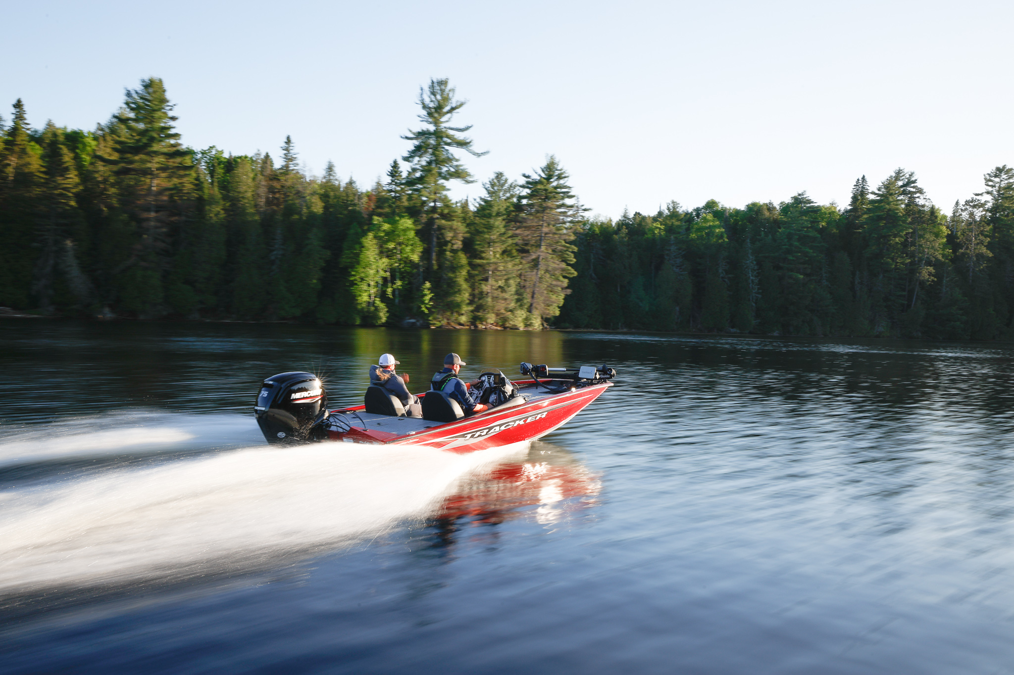 Two people on a fast boat moving across a lake with trees in the background.