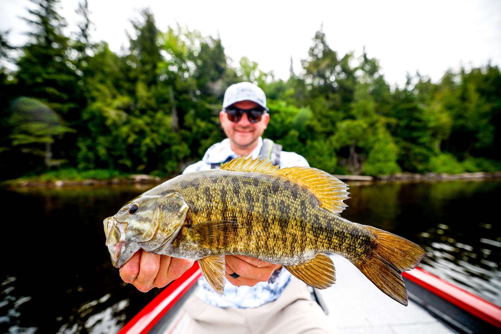 A man on a boat on a lake holding up a fish, boating in Alberta concept.