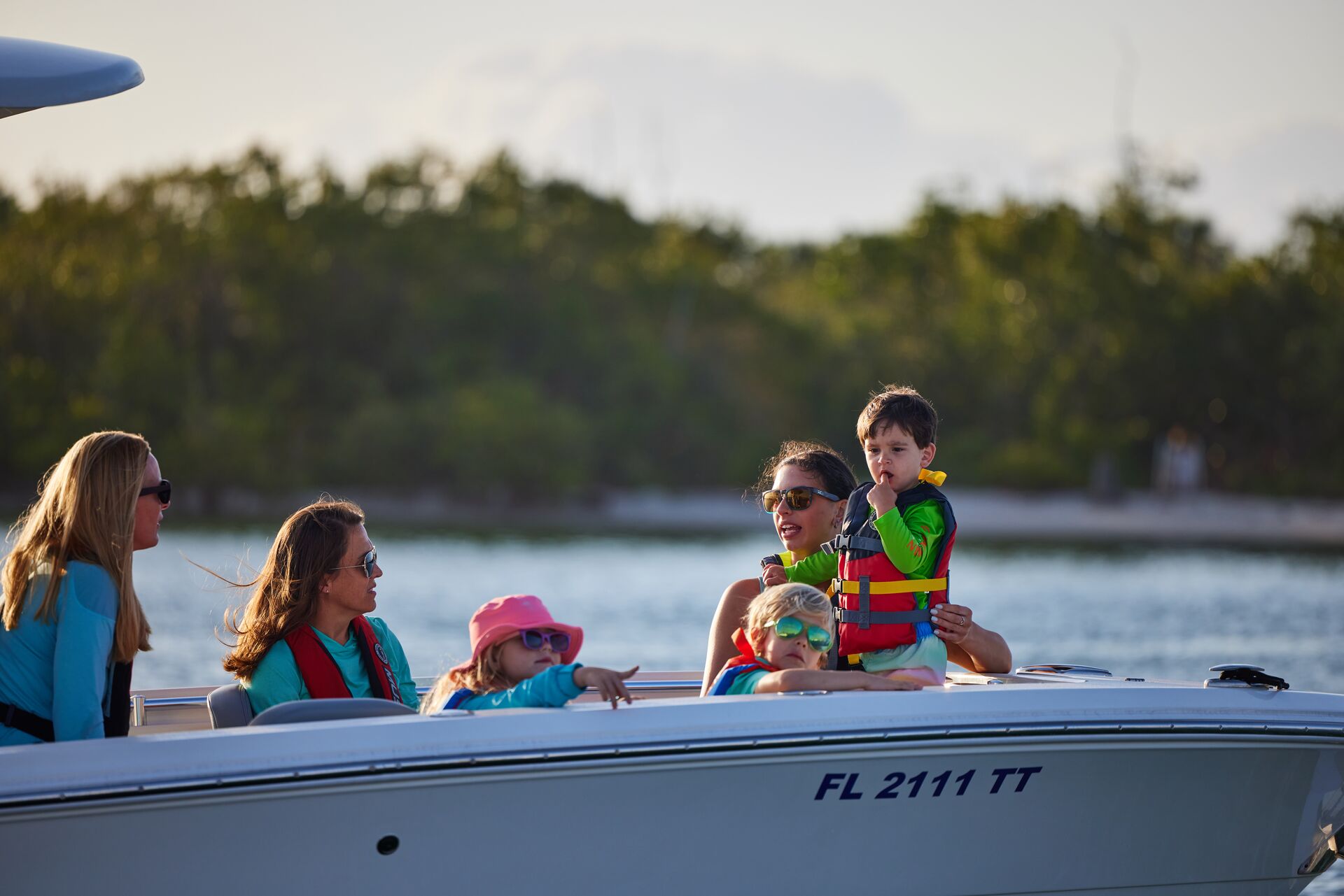 Women and children wearing life jackets on a boat on a lake.