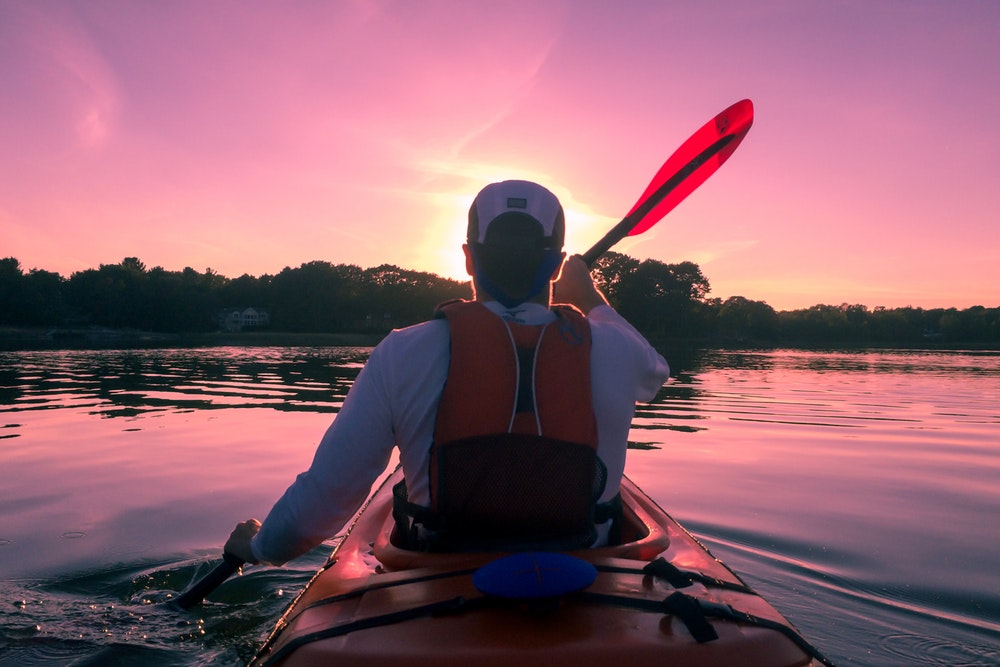 A guy paddling a kayak while wearing a life jacket, water activities in New York concept.