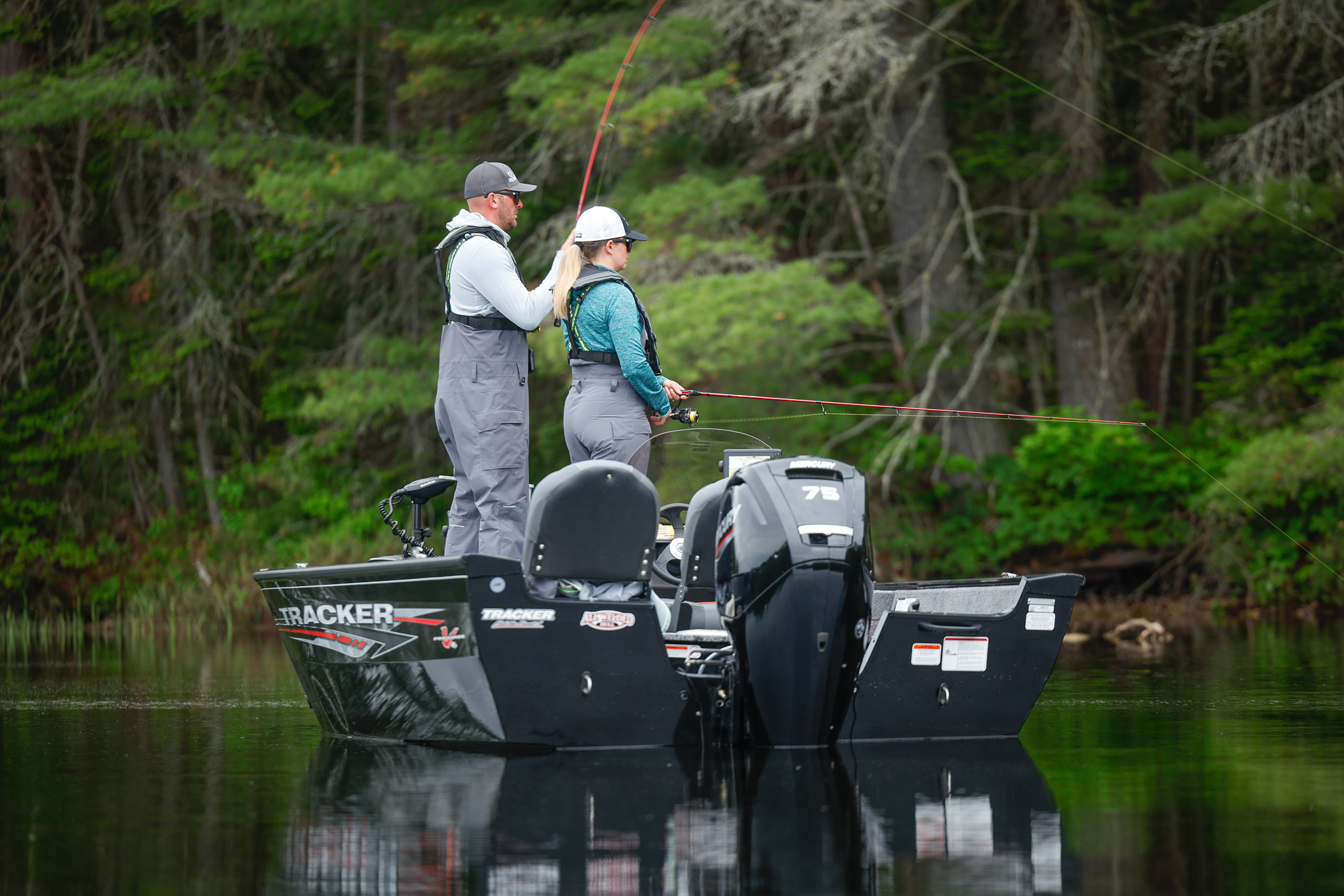 Two people with lines in the water to fish from a boat.