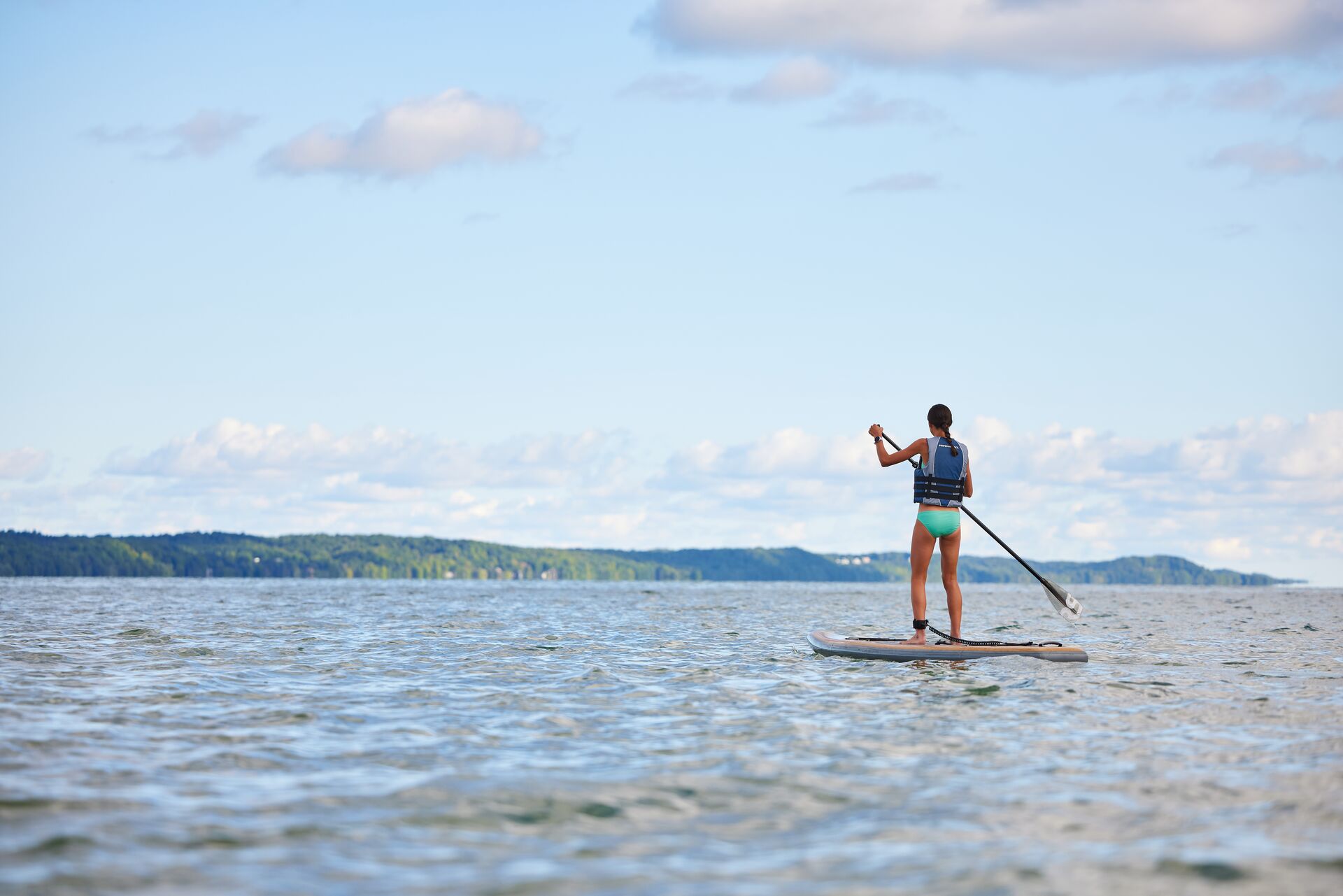 A girl wears a life jacket while on a paddle board on the water, follow South Dakota boating laws concept.