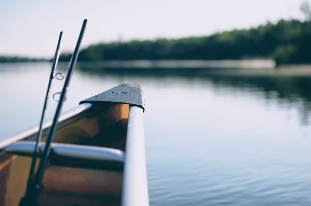 A fishing rod at the front of a boat on calm waters.