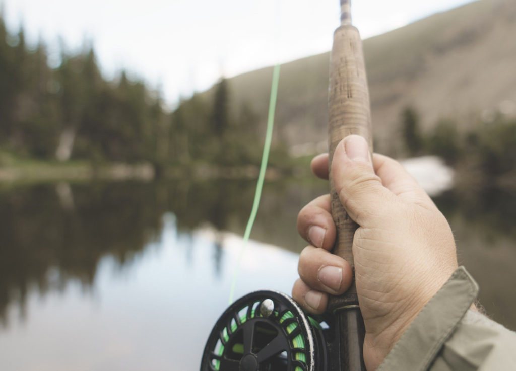 A hand holding a fishing rod and reel over the water, bass fishing concept. 