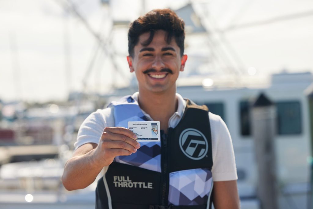 A smiling man in a lifejacket holding a boater safety card, boating on Lake Tahoe safely concept.