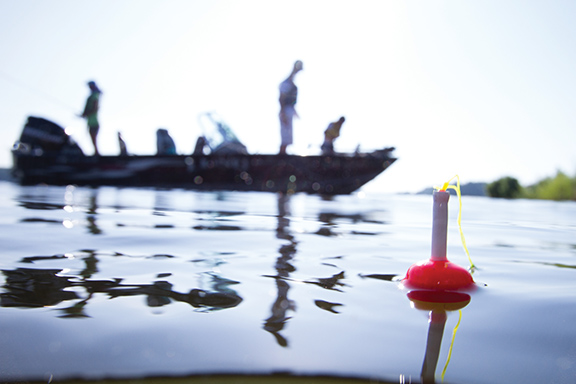 A fishing lure bobs on the water with people on a boat in the background.