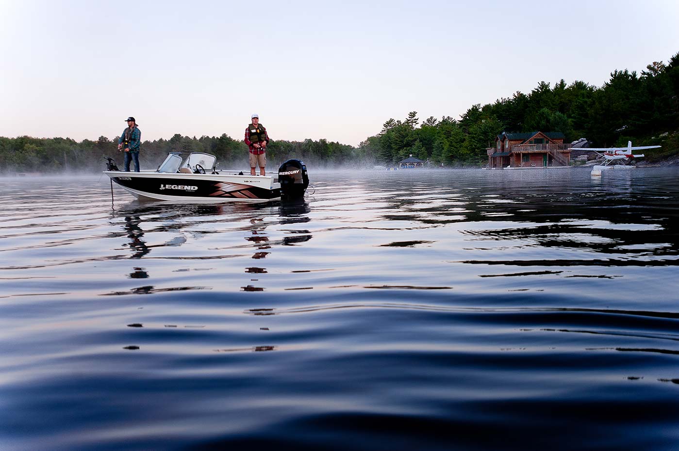 Two men fishing from a boat on calm waters. 