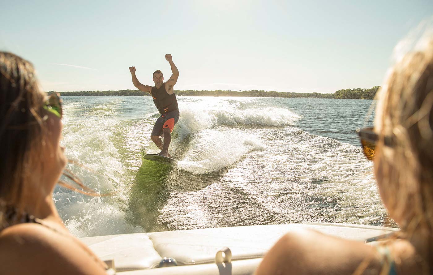 Two girls watching a guy wakesurf behind a boat, boating in Alaska concept.