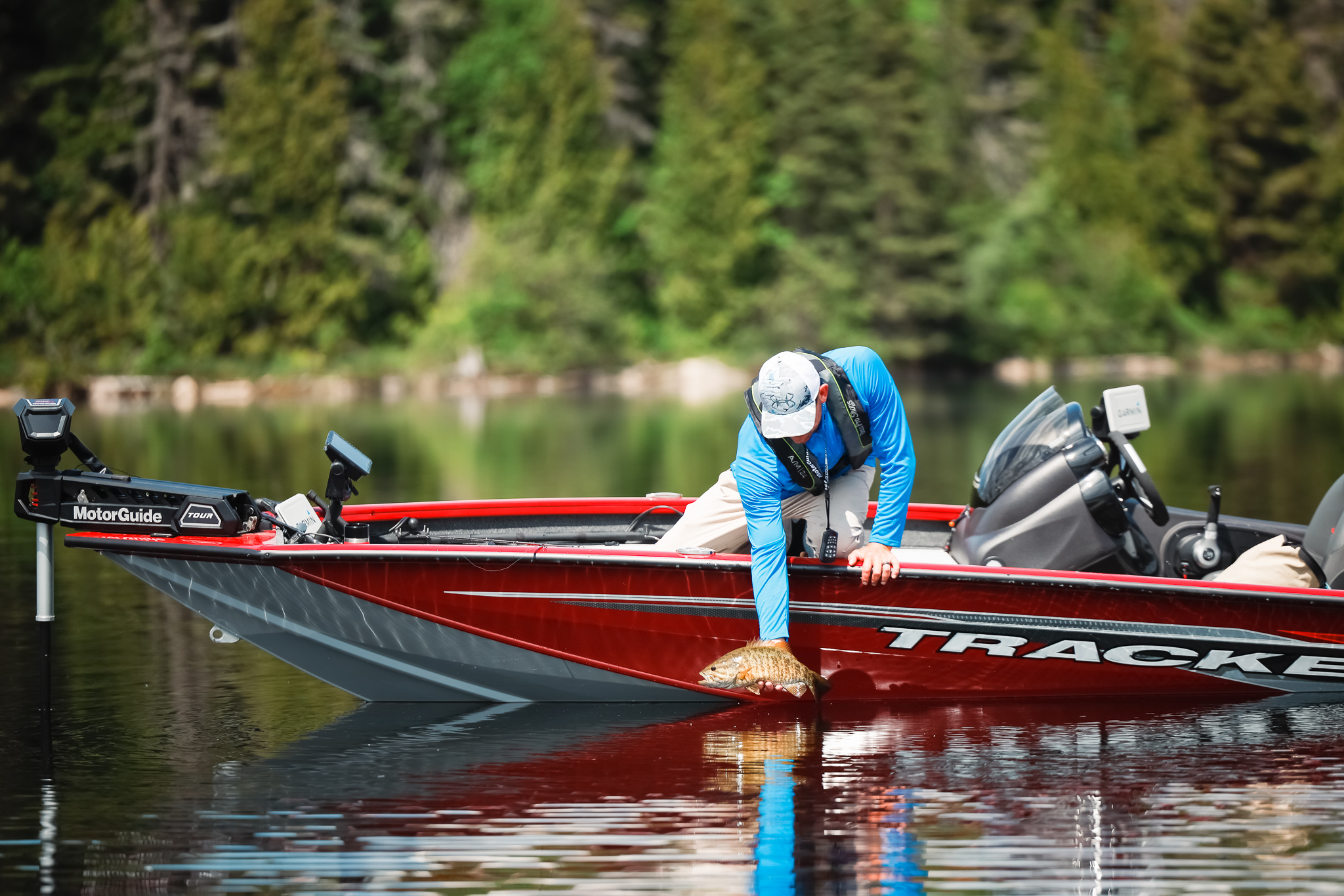 An angler scoops a fish out of the water while leaning over the edge of a boat.
