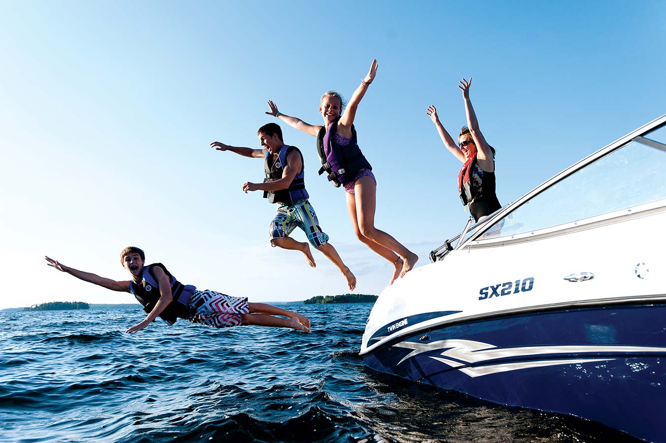 Kids wearing life jackets while jumping from boat into water, know Utah boating laws concept. 