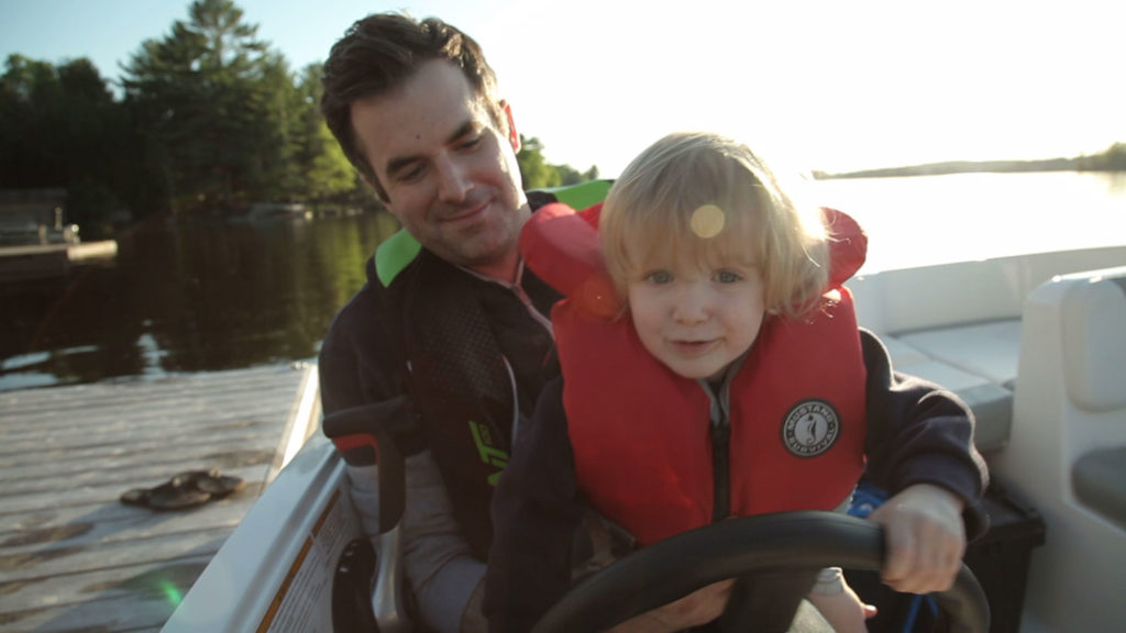 A man and boy wearing life jackets behind the helm of a boat, boating access concept.