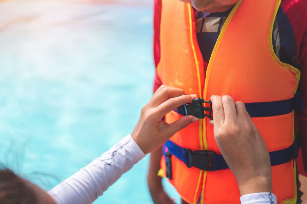 Hands helping fasten a life jacket on a child, New York life jacket laws concept.