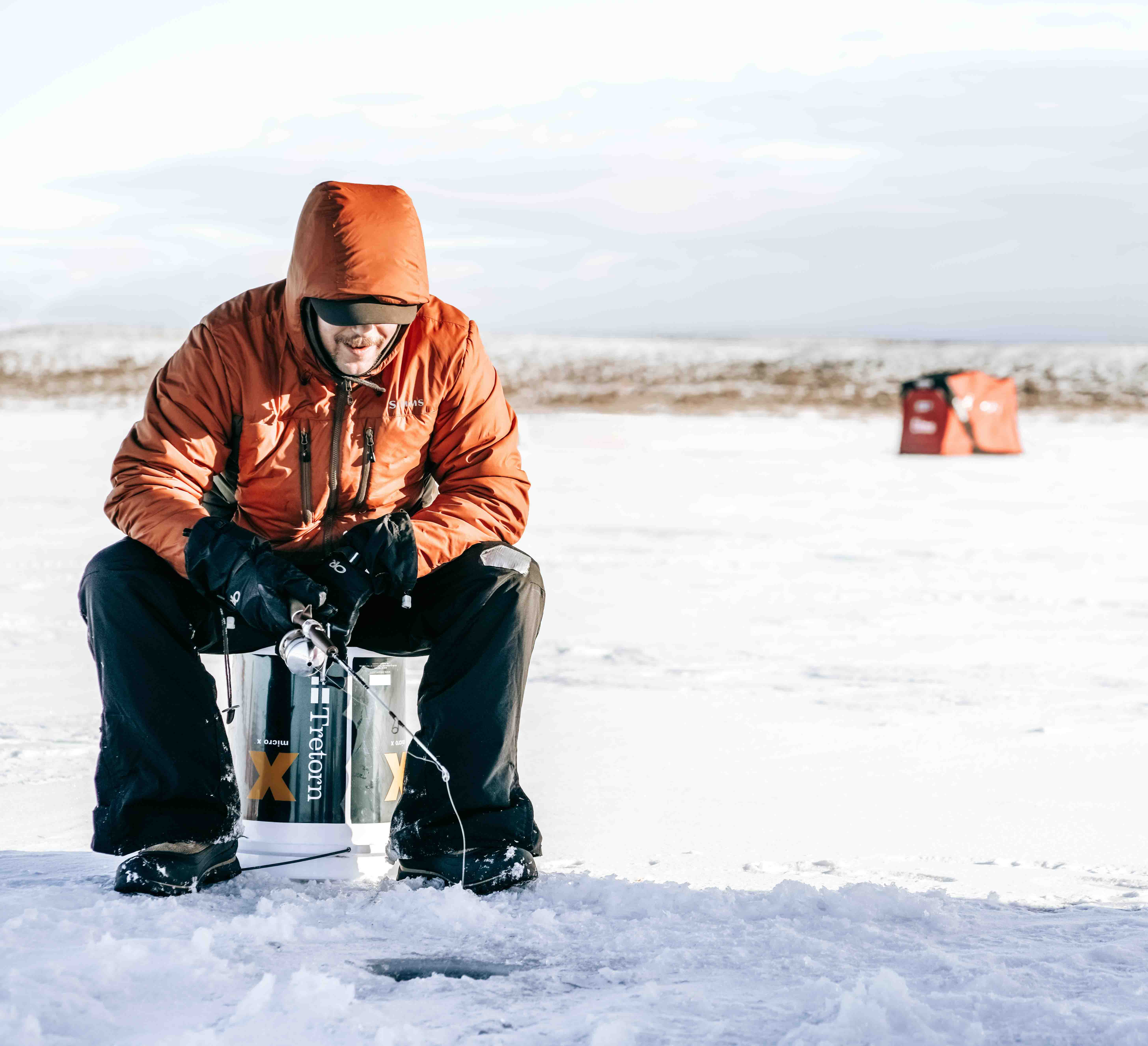 A man in a coat sitting over a hole in the ice, beginner's guide to ice fishing concept. 