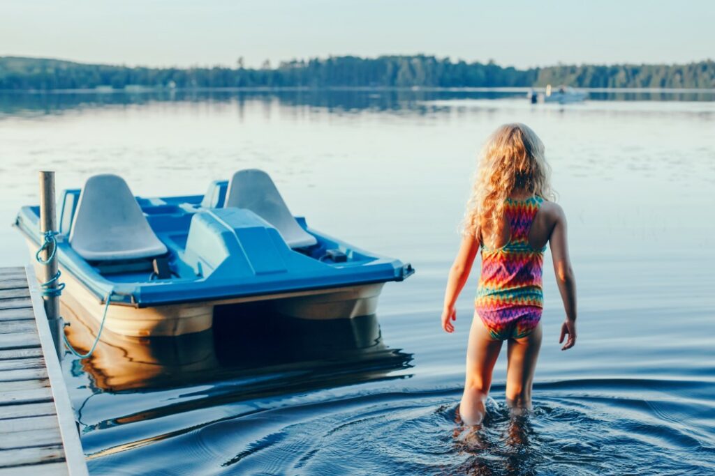 Child swimming in Lake Muskoka next to a paddle boat, boating in Ontario concept.