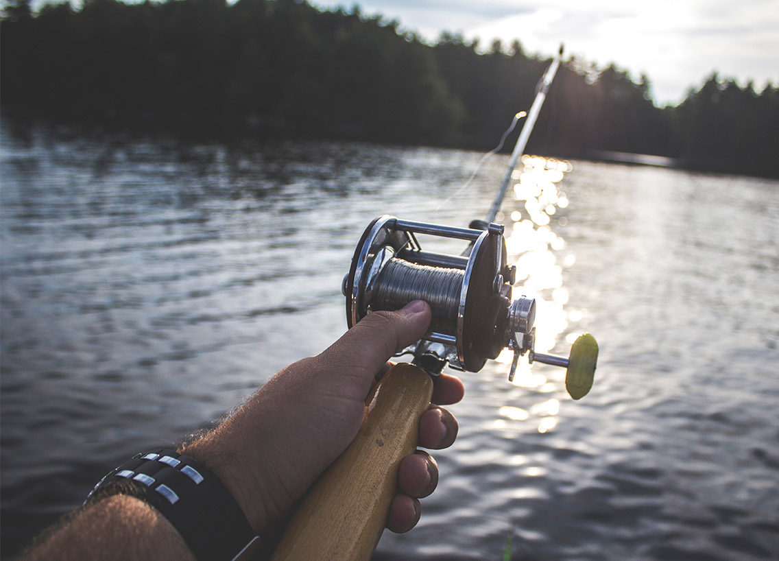 Close-up of a hand casting a rod and reel into the water. 