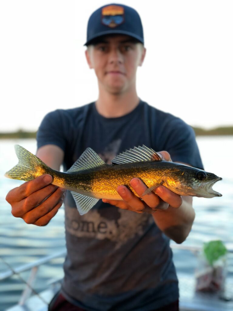 A young man holds up a fish, fishing in Alberta concept. 