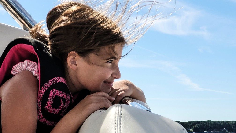 A girl wearing a life jacket while looking over the side of a boat, boating in the Yukon concept.