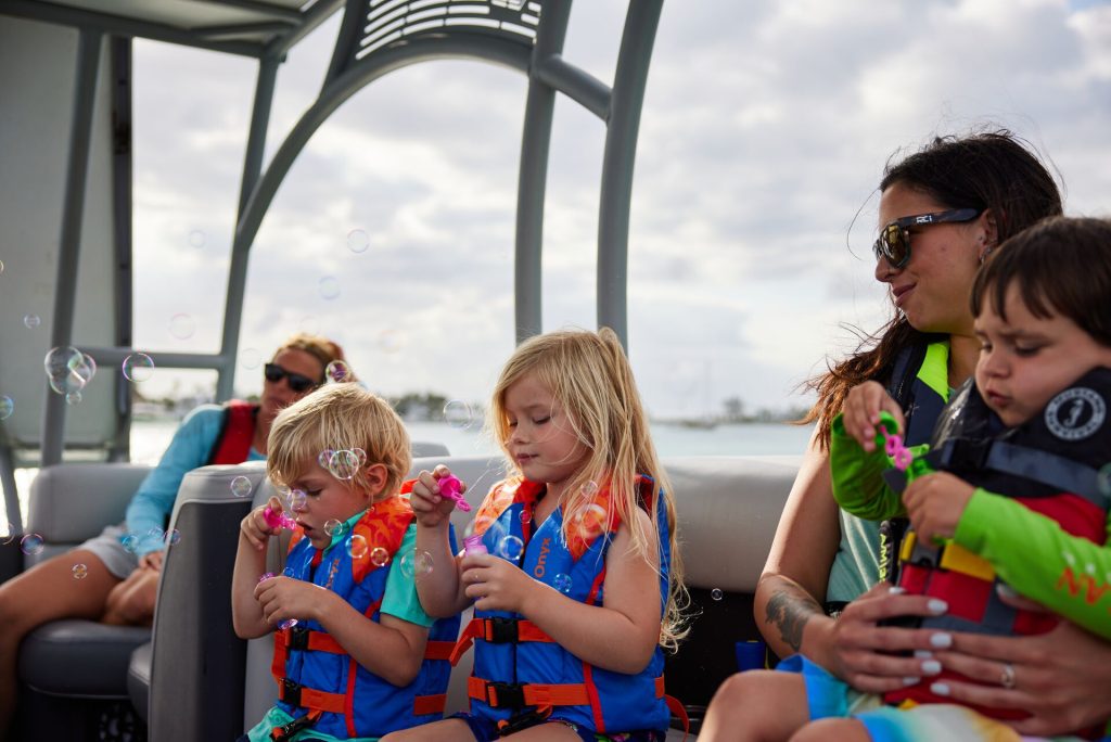 Kids and a woman blowing bubbles while wearing lifejackets on a boat, boat with kids concept.