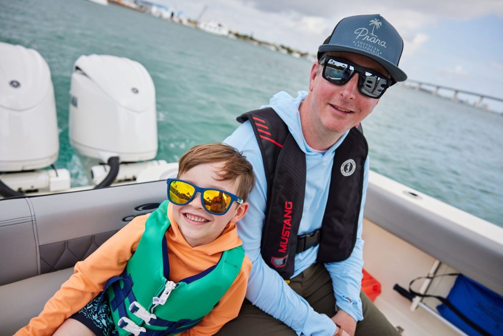 A man and boy smile and wear life jackets on a boat, boating in Georgia concept.