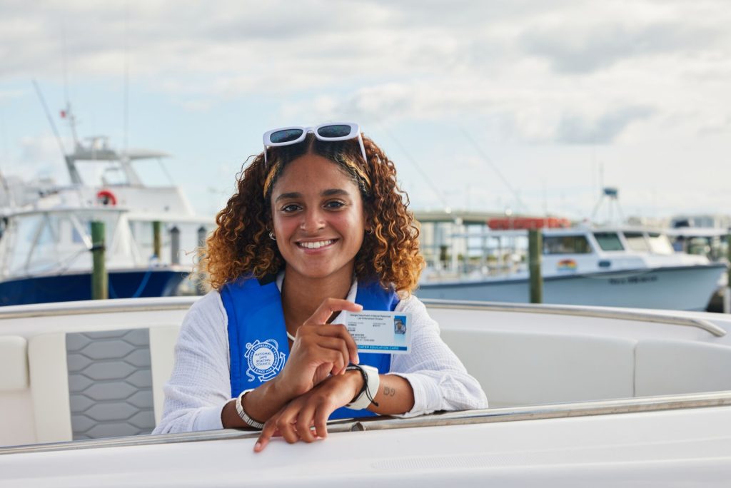 Smiling woman wearing a life jacket holding a boater education card on a boat. 