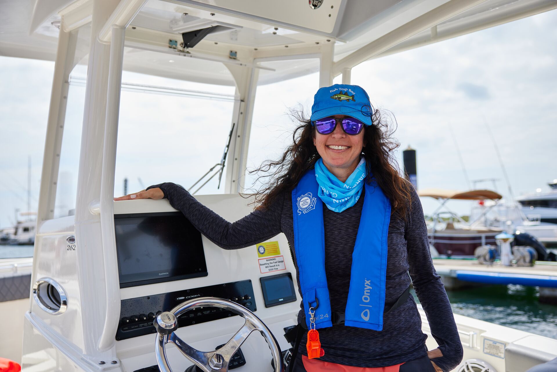 A smiling woman wearing a life jacket at the helm of a boat.