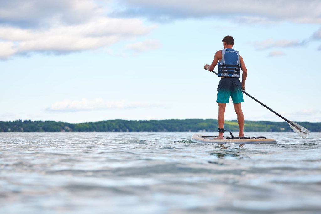 A boy on a paddle board while enjoying the water and wearing a life jacket.