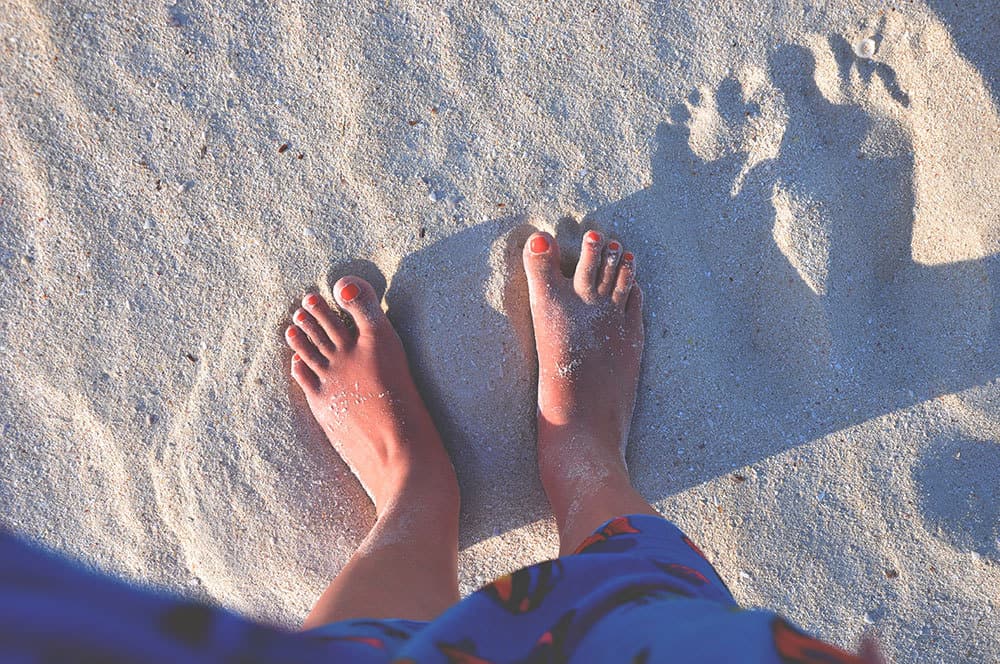 Looking down at two feet in the sand. 