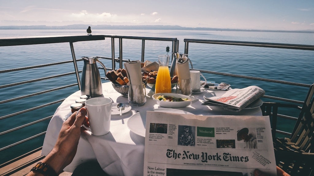 A view of someone reading a newspaper and eating brunch on a boat. 