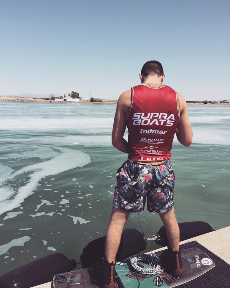 A guy on a wakeboard stands at the back of a boat.