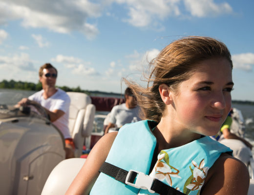 girl sitting in boat with lifejacket on and father in background