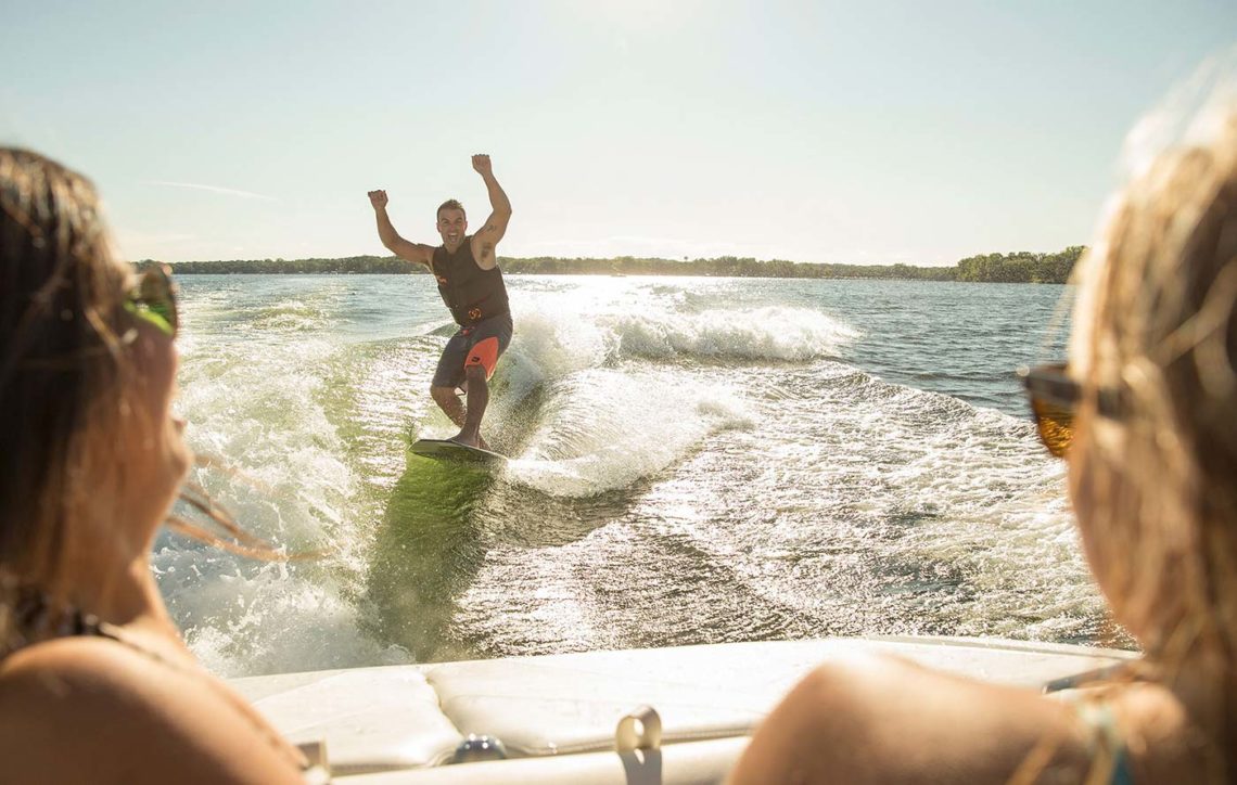 Dude wake surfing with hands in the air