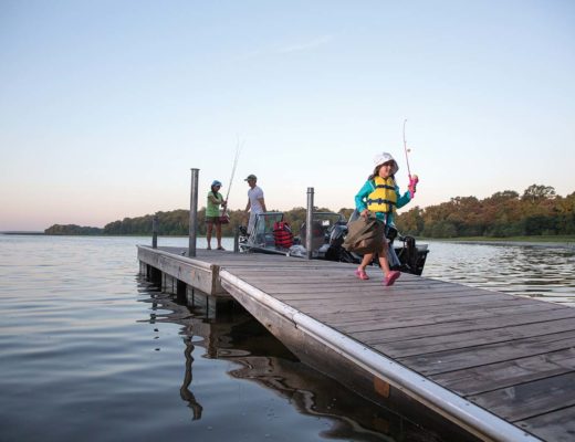 Girl carrying tackle box on dock with parents in background