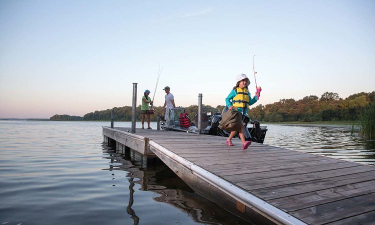 Girl carrying tackle box on dock with parents in background