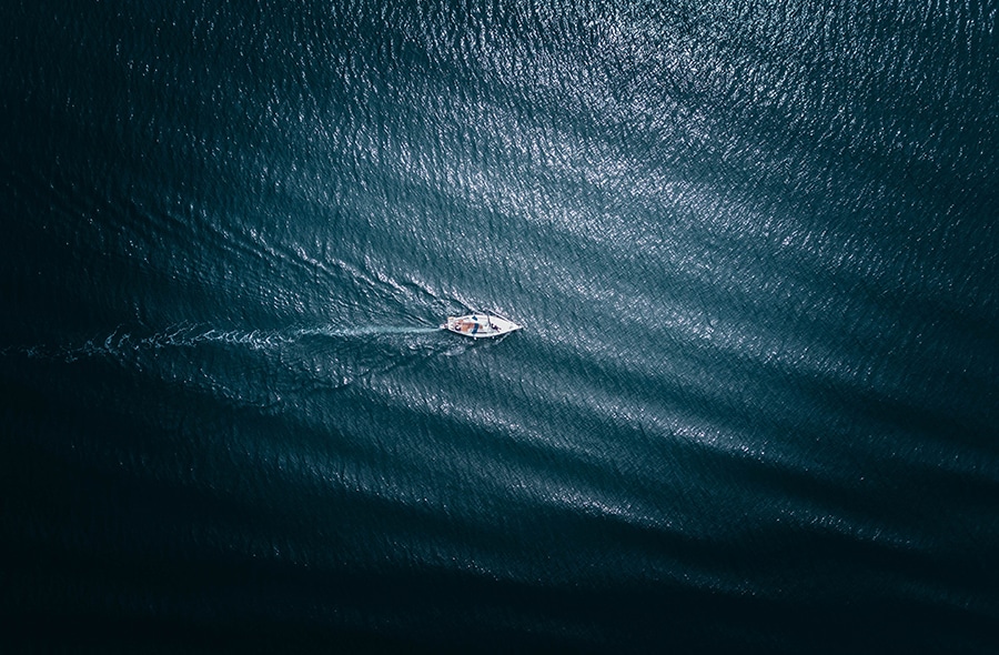 Aerial shot of lone sailboat on choppy water.