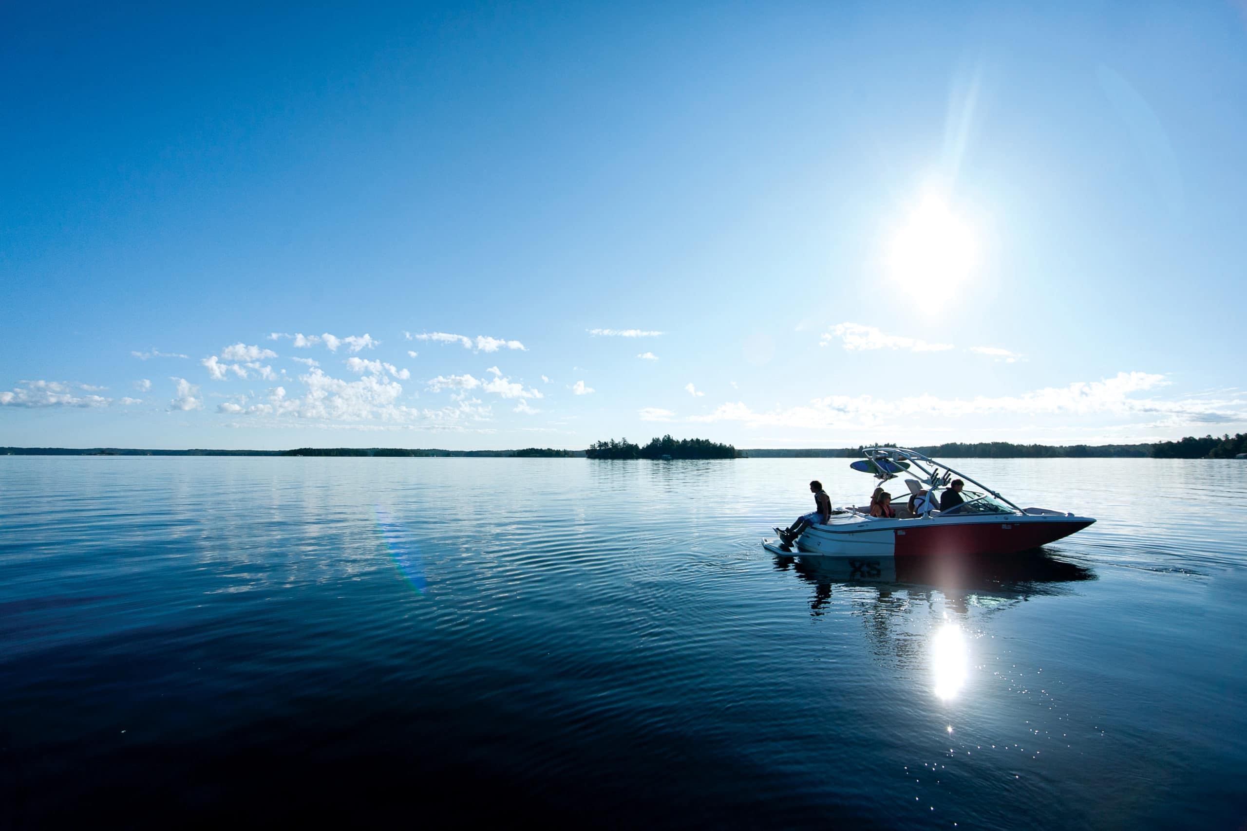 Wakeboarder sitting on bow of boat looking out over calm lake.