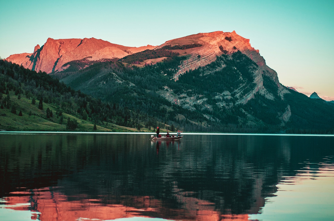 Three people fishing from boat on calm lake.