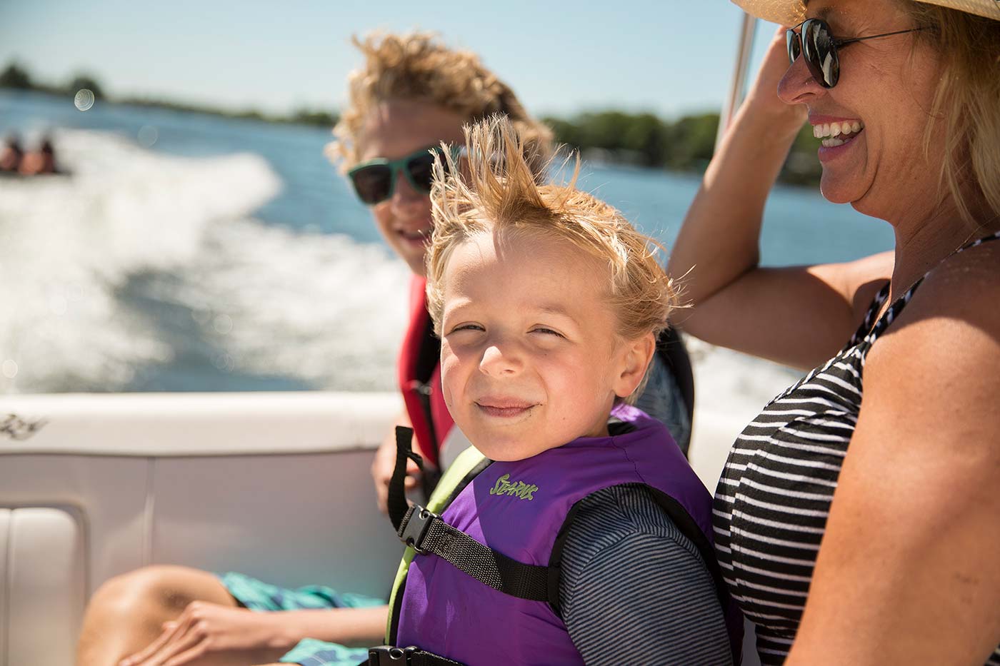 two kids in lifejackets sitting with grandparent on boat